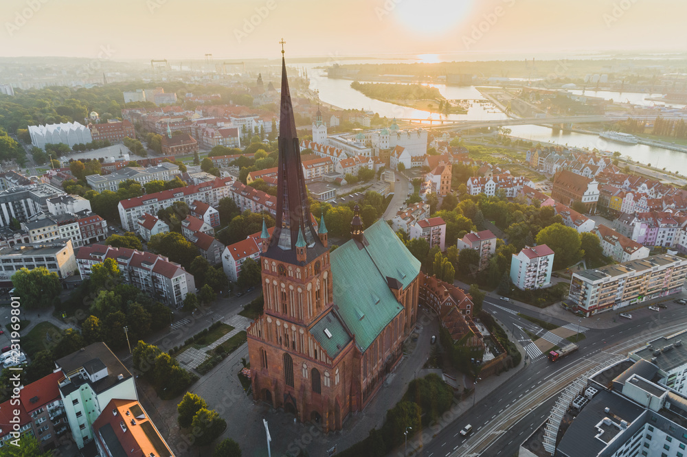 Widok z lotu ptaka na Katedrę św. Jakuba w Szczecinie o zachodzie słońca, z panoramą centrum miasta, Odrą i ciepłym złotym światłem nad horyzontem