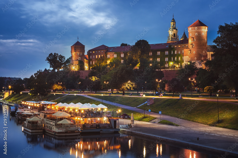 Nocna panorama Wzgórza Wawelskiego z iluminowanym zamkiem, Wisłą i cumującymi barkami w ciepłym złotym świetle na granatowym niebie - obraz drukowany na płótnie