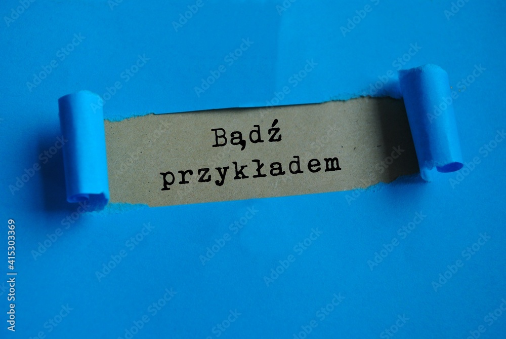 Napis 'Bądź przykładem' odsłonięty na beżowym papierze przez rozerwane niebieskie tło, symbolizujący przełomowe odkrycie własnego potencjału