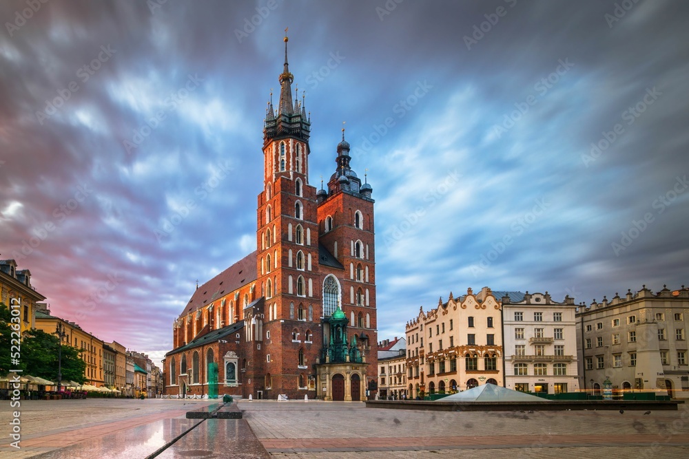 Fotografia gotyckiej wieży Bazyliki Mariackiej z cegły na tle błękitnego nieba z chmurami, niska perspektywa - obraz drukowany na płótnie